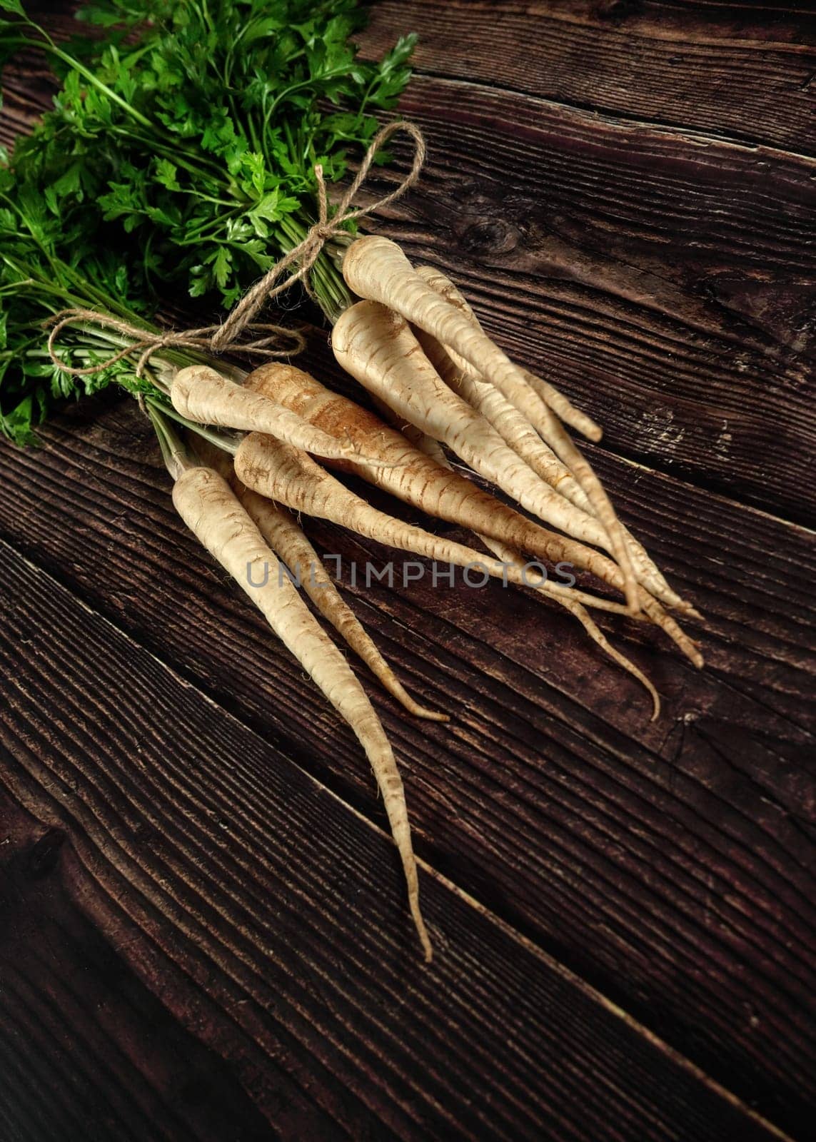 Bunch of parsnips with green leaves on dark wooden desk. by Ivanko