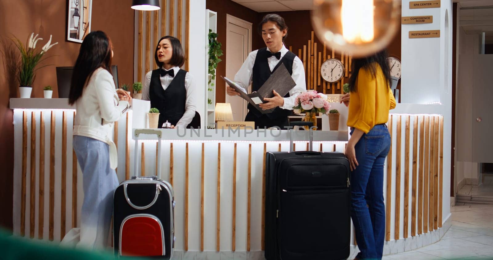 Hotel employees greeting customers at front desk in lobby, preparing for check in process. Receptionist looking for room reservation details, travelers confirming booking accommodation.