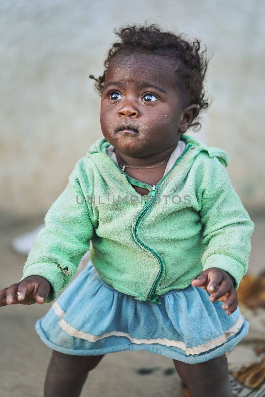 Ranohira, Madagascar - April 29, 2019: Malagasy girl toddler, in torn clothes, sweater inside out, barely standing on ground, balancing trying not to fall. Most population in Madagascar is very poor