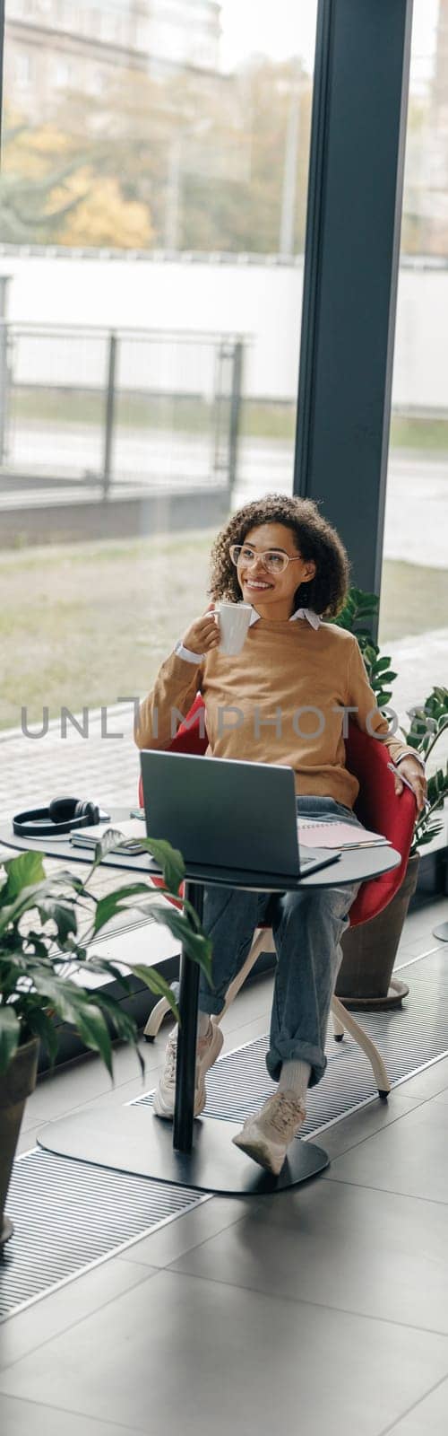 Smiling business woman in eyeglasses have a coffee break during working on laptop in cozy cafe