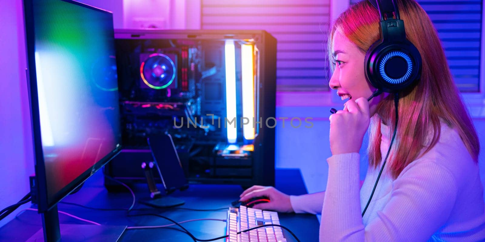 Happy Gamer endeavor plays online video games tournament with computer neon lights, young woman wearing gaming headphones intend to do playing live stream games online at home