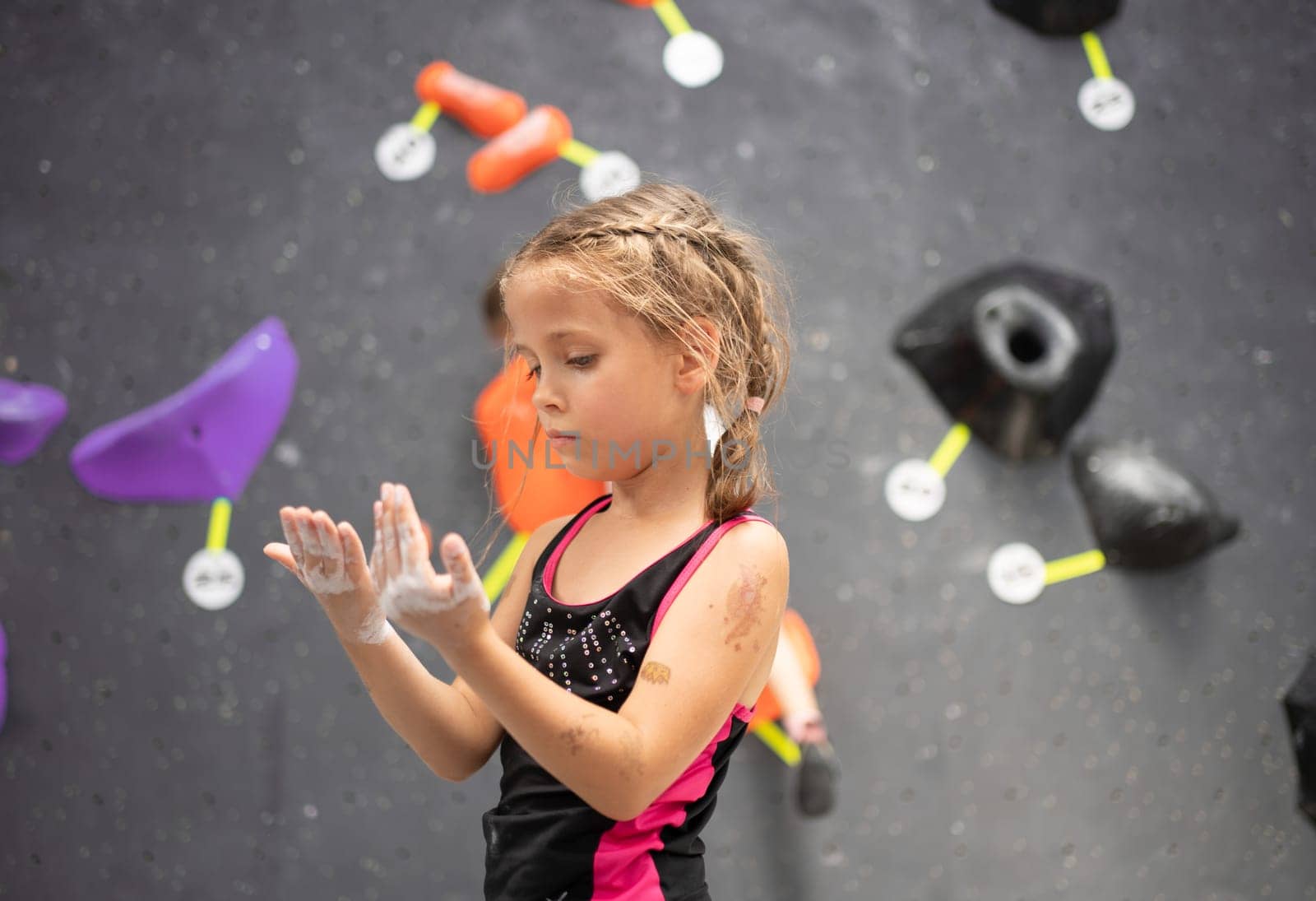 Cute adorable girl climber looking at hands coated with powder chalk magnesium. Determined child preparing for rock climbing in sports center. Fitness and healthy lifestyle.