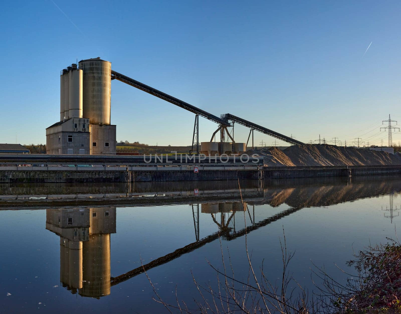 Riverside Manufacturing Hub. Eco-Friendly Technology and Production. Explore the synergy of technology and production at the Riverside Manufacturing Hub, nestled by the river. Witness the balance between industry and the environment, showcasing the integration of sustainable practices. This image captures the essence of eco-friendly manufacturing and its harmonious coexistence with the surrounding natural beauty.