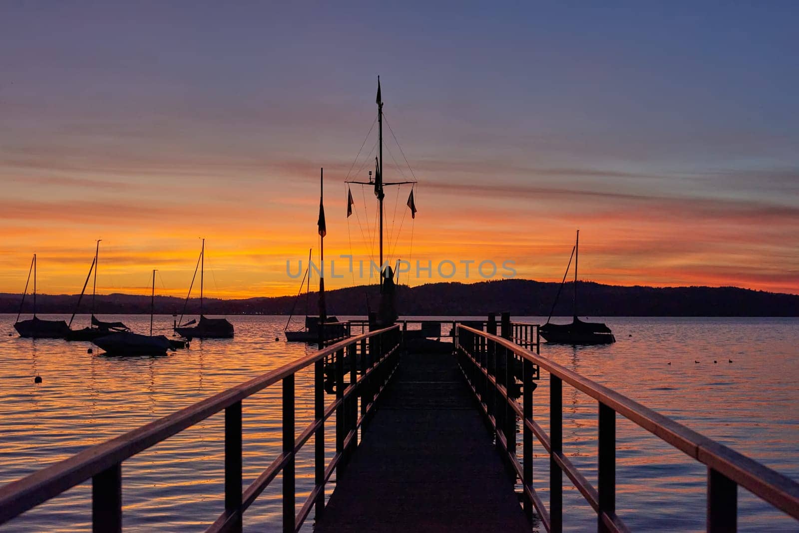 Bodensee Lake Panorama. Evening, twilight, setting sun, picturesque landscape, serene waters, boats and yachts at the dock, beautiful sky with clouds reflecting in the water, riverside at dusk, showcasing the coexistence of technology and production with the environment.