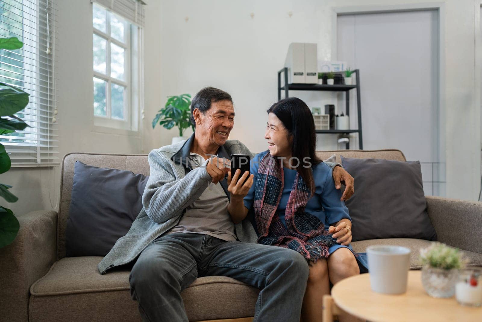 Retired elderly couple sits on couch using mobile together and relax in their home. Senior Activity Concept.