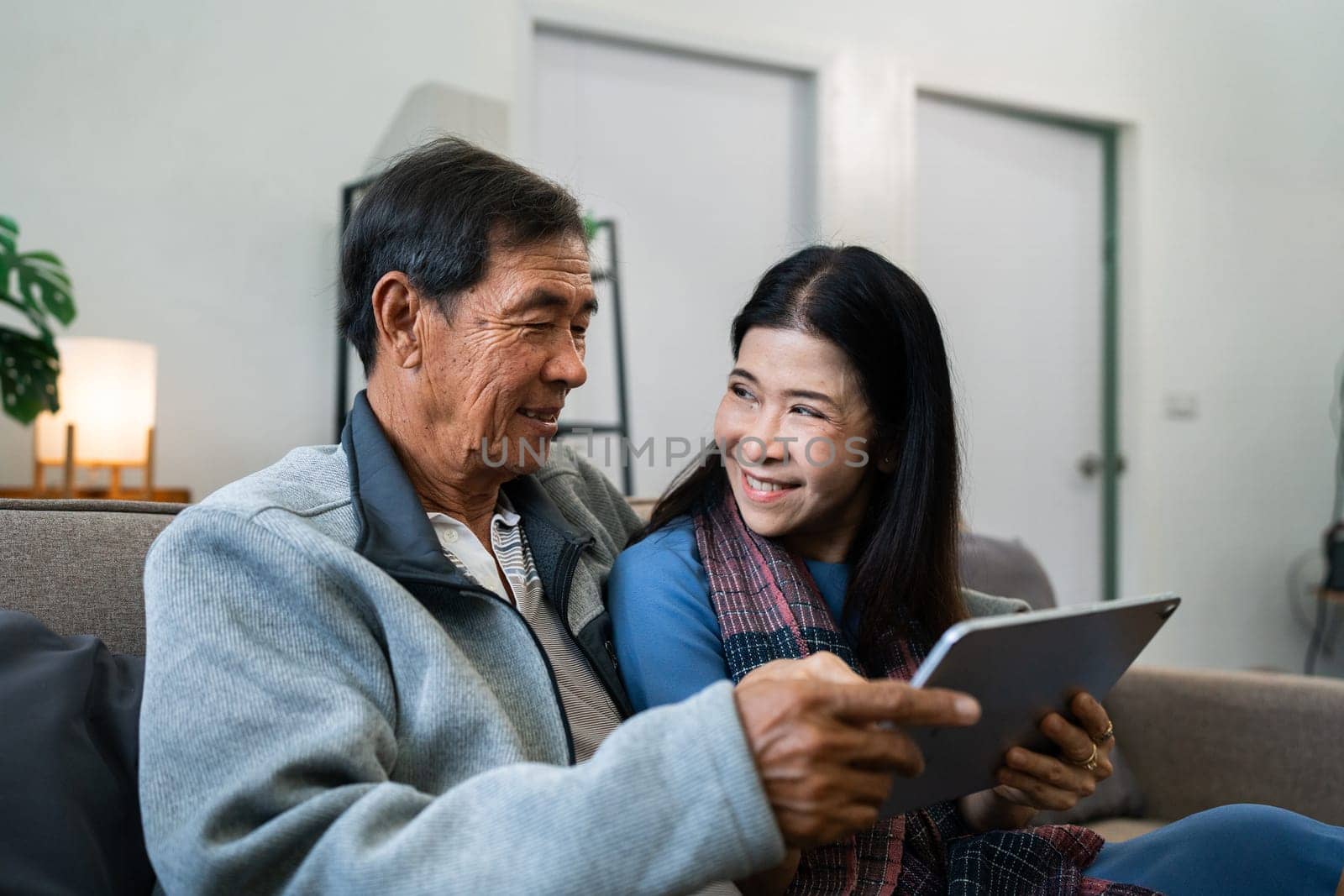 Retired elderly couple sits on couch using tablet together and relax in their home. Senior Activity Concept.