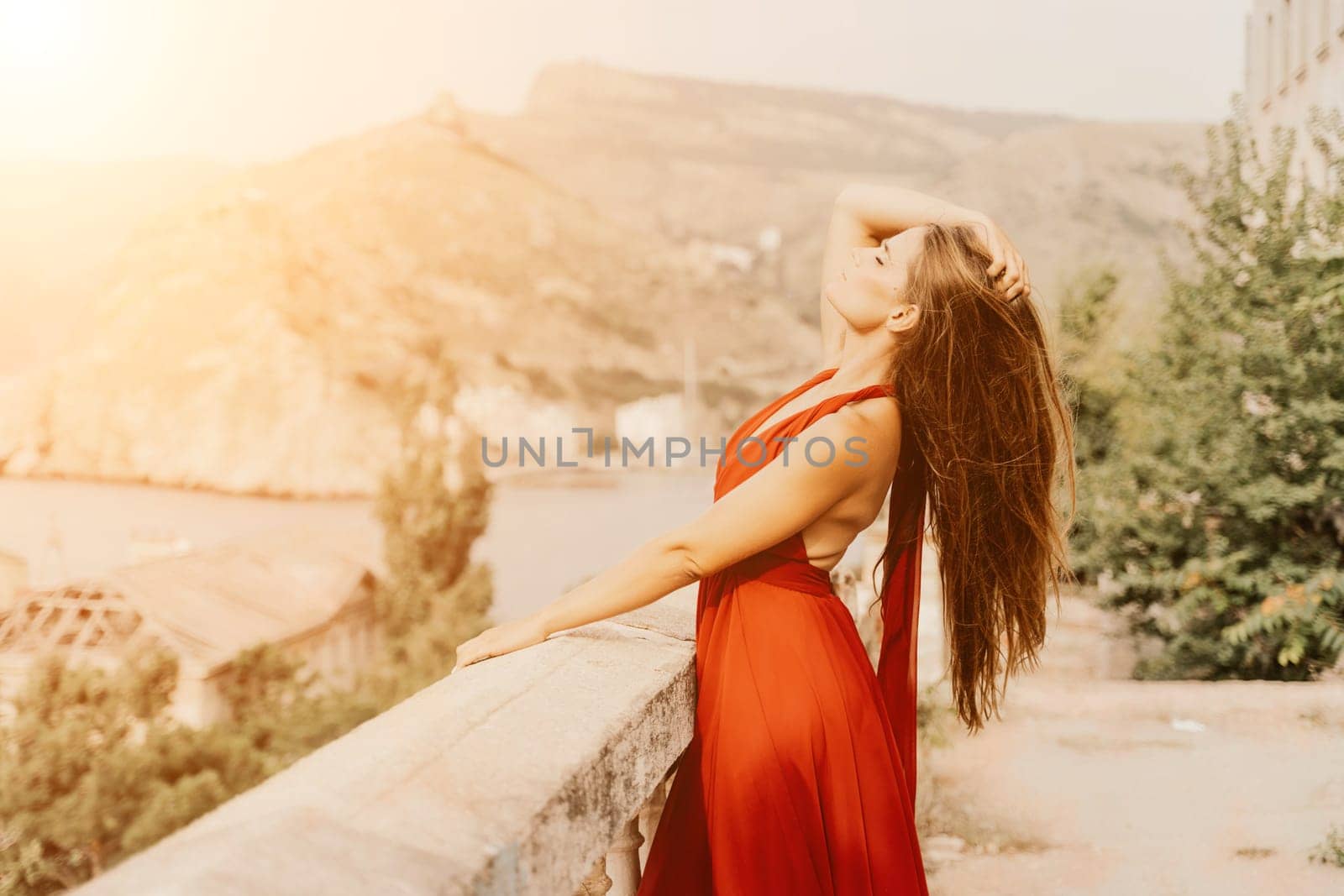 Woman red dress. Summer lifestyle of a happy woman posing near a fence with balusters over the sea. by Matiunina