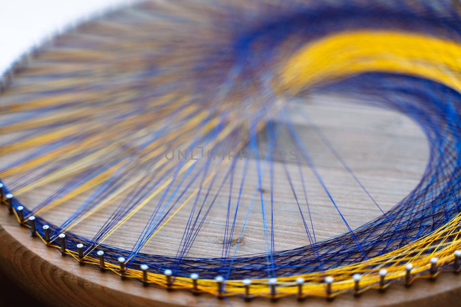 Colored thread mandala on a wooden board with nails. Mandala Moon Harmony Sun esotericism and psychology pictures from yellow and blue silk threads. by Matiunina