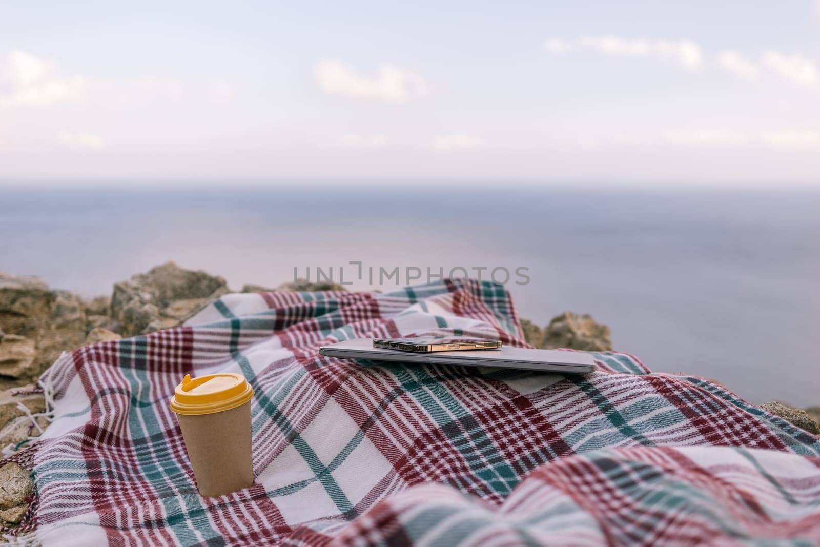 Laptop coffee on blanket with ocean view. Illustrating serene outdoor laptop use. Freelancer enjoying their time outdoors while working or browsing the internet