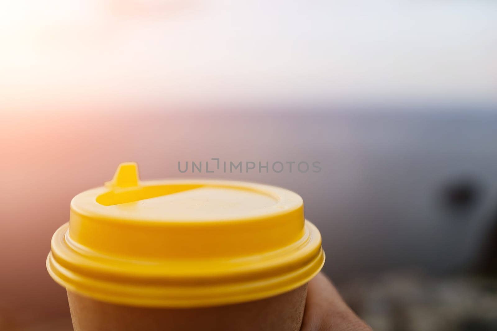 Yellow cup with lid, coffee against a backdrop of a blue sky and sea. Illustrating cup and beverage.