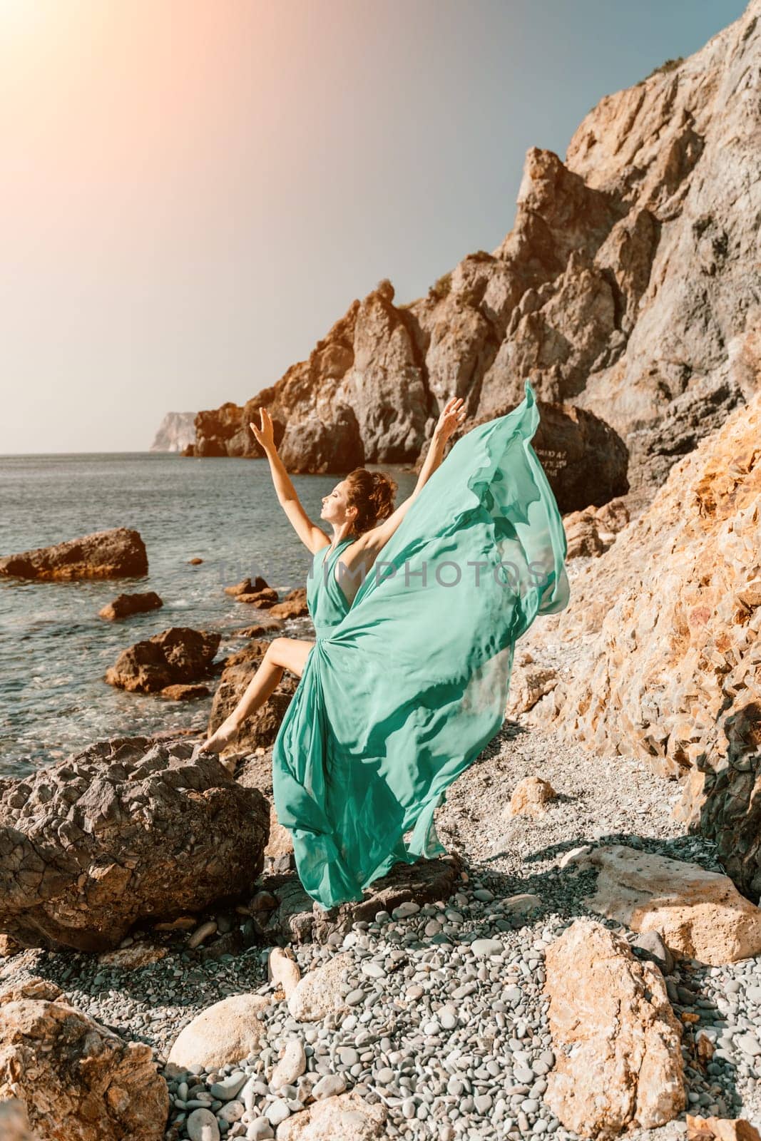 Woman green dress sea. Woman in a long mint dress posing on a beach with rocks on sunny day. Girl on the nature on blue sky background. by Matiunina
