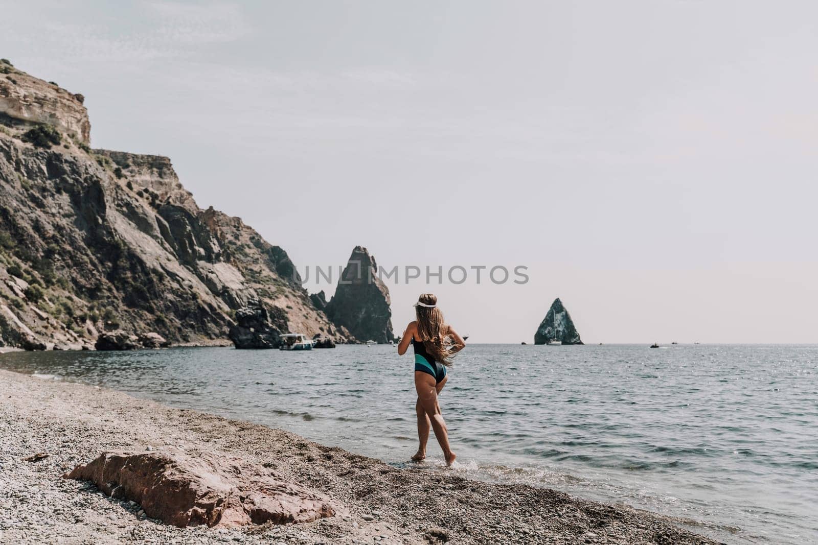 Woman beach vacation photo. A happy tourist in a blue bikini enjoying the scenic view of the sea and volcanic mountains while taking pictures to capture the memories of her travel adventure