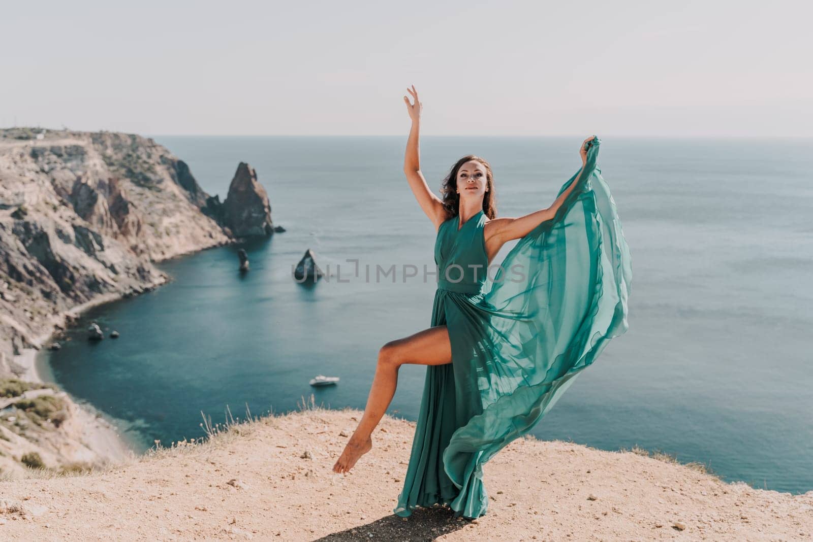 Woman green dress sea. Female dancer posing on a rocky outcrop high above the sea. Girl on the nature on blue sky background. Fashion photo. by Matiunina