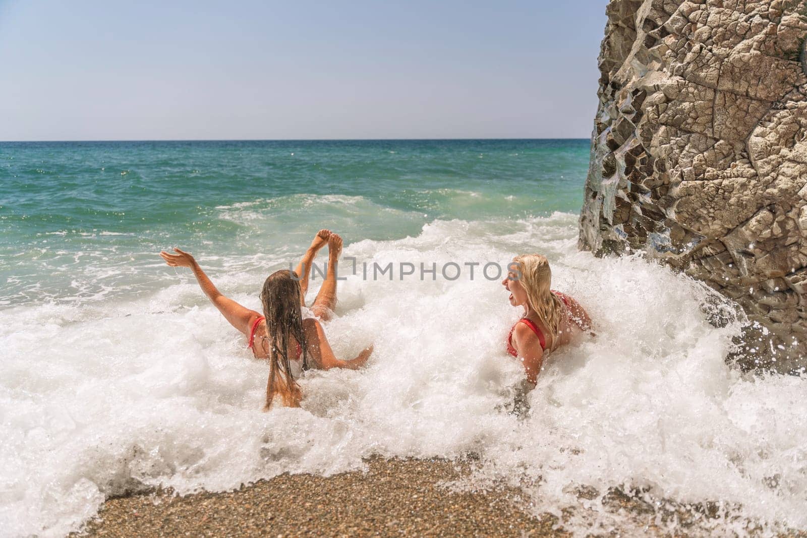 Women ocean play. Seaside, beach daytime, enjoying beach fun. Two women in red swimsuits enjoying themselves in the ocean waves