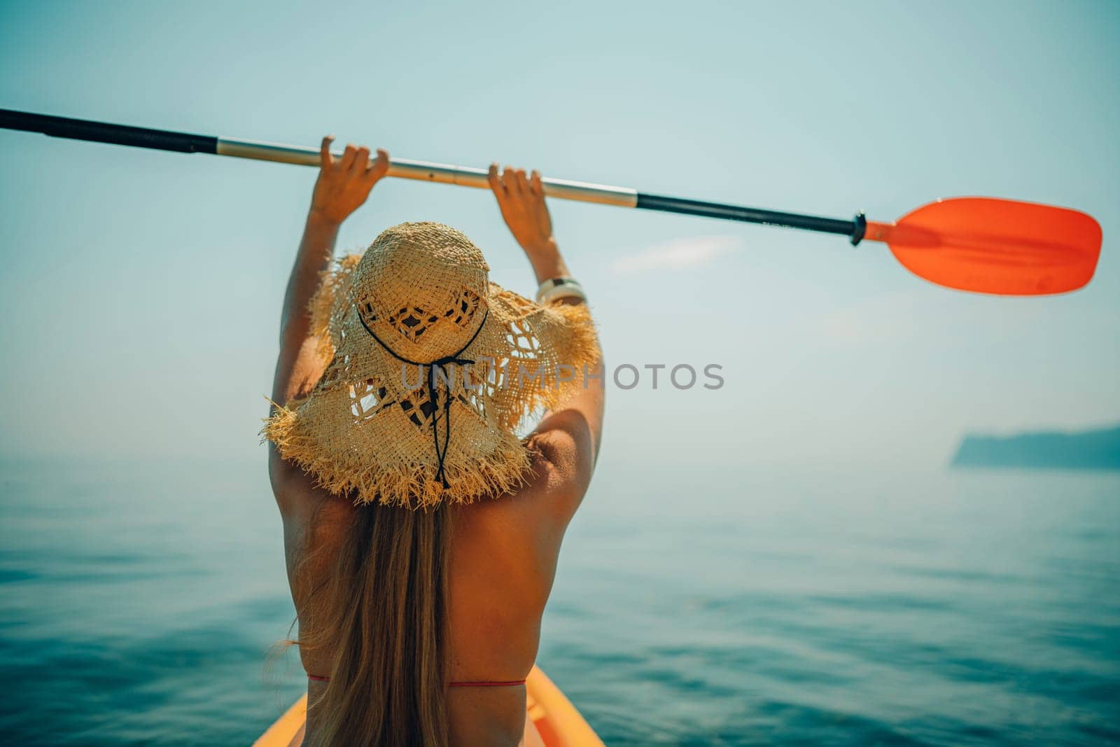 Woman in kayak back view. Happy woman with long hair in a swimsuit and hat floating in kayak on the sea. Summer holiday vacation. Summer holidays vacation at sea