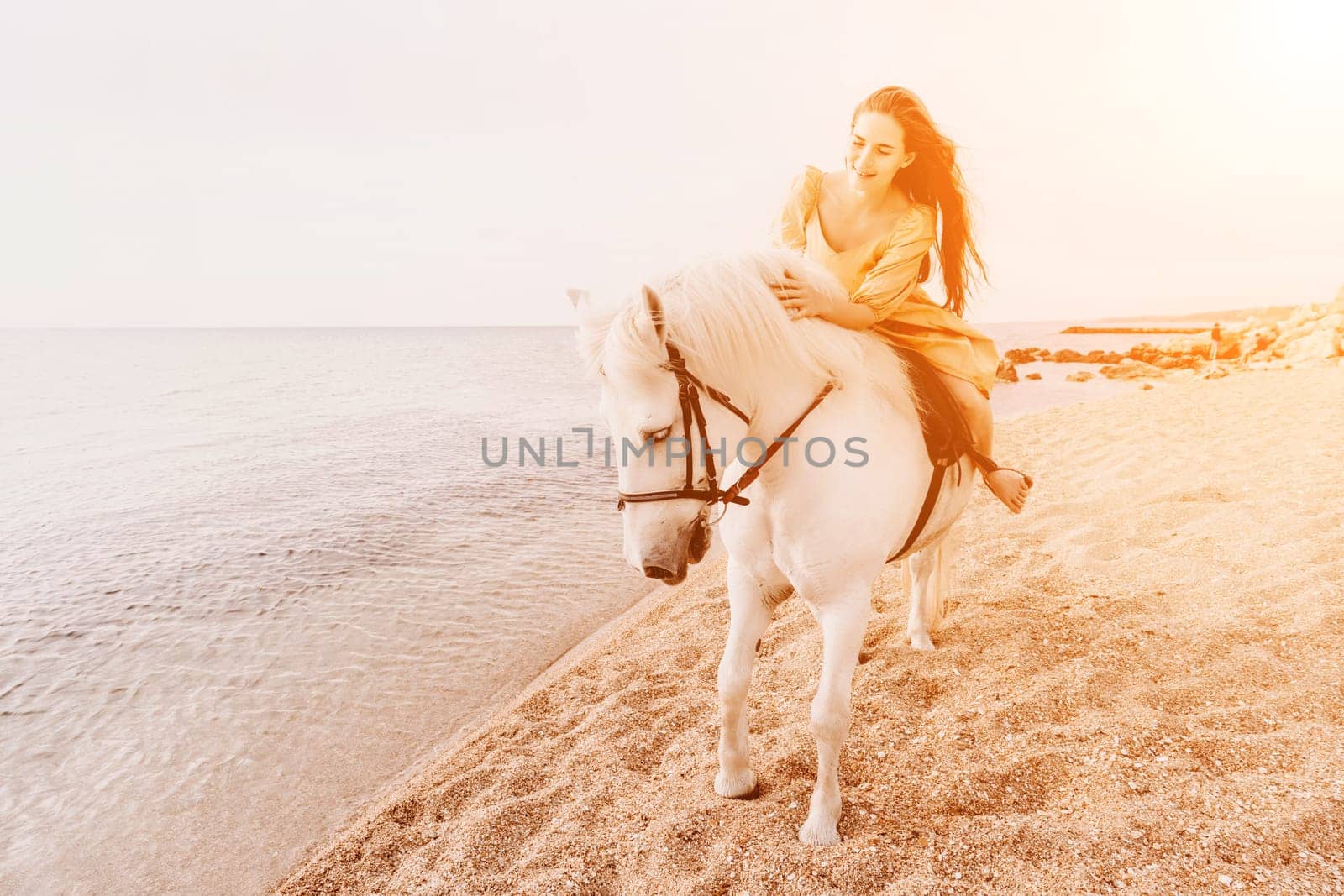 A white horse and a woman in a dress stand on a beach, with the sky and sea creating a picturesque backdrop for the scene