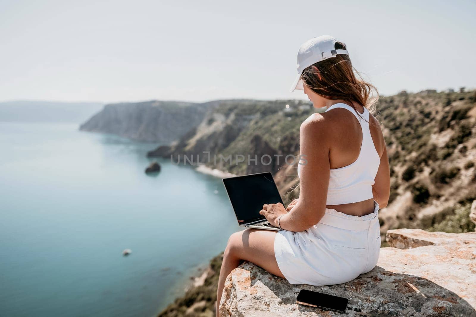 Digital nomad, Business woman working on laptop by the sea. Pretty lady typing on computer by the sea at sunset, makes a business transaction online from a distance. Freelance, remote work on vacation by panophotograph