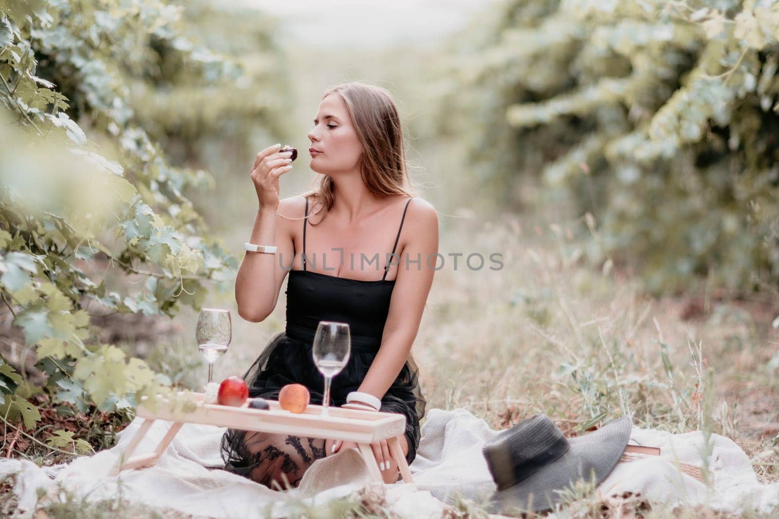 Woman picnic vineyard. Happy woman with a glass of wine at a picnic in the vineyard, wine tasting at sunset and open nature in the summer. Romantic dinner, fruit and wine. by panophotograph