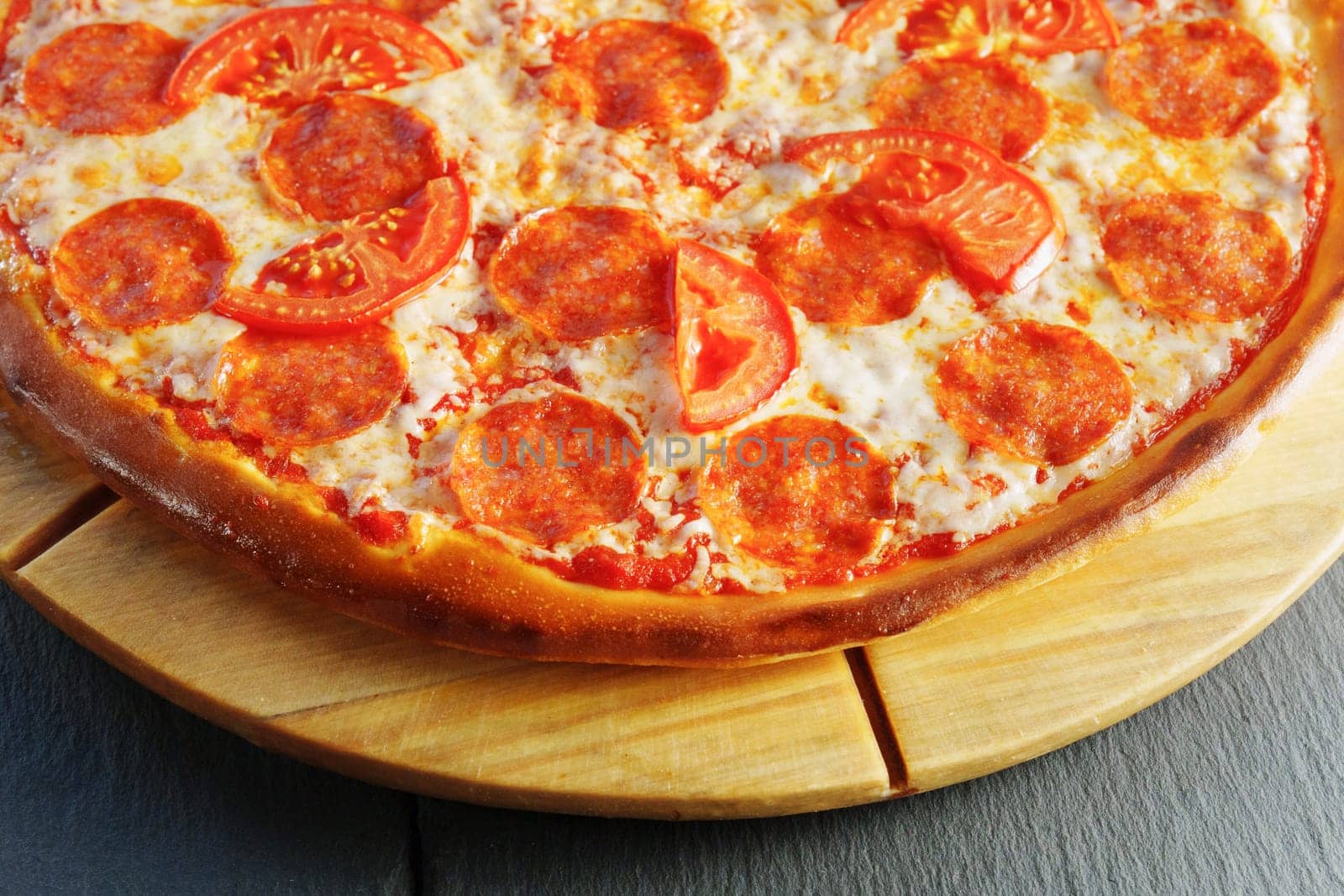 Baked pepperoni and tomato pizza sits invitingly on a wooden serving board.