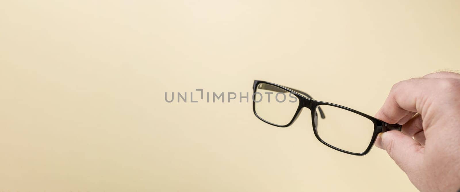 Hand holding black framed prescription glasses in front of yellow background