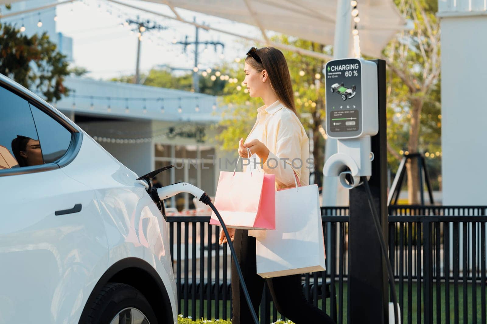 Young woman holding shopping bag recharge EV car. Expedient by biancoblue