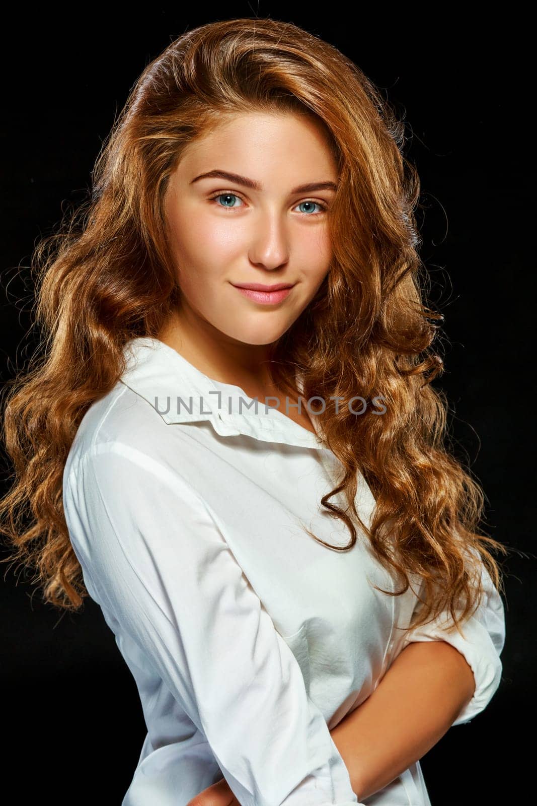 Portrait beautiful young brunette woman with wavy hair in white clothes, looking at the camera, isolated on dark background