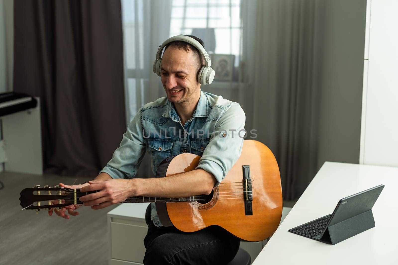 Man wearing headphones, sitting at desk with guitar, happy musician artist reading good comments in social networks. High quality photo