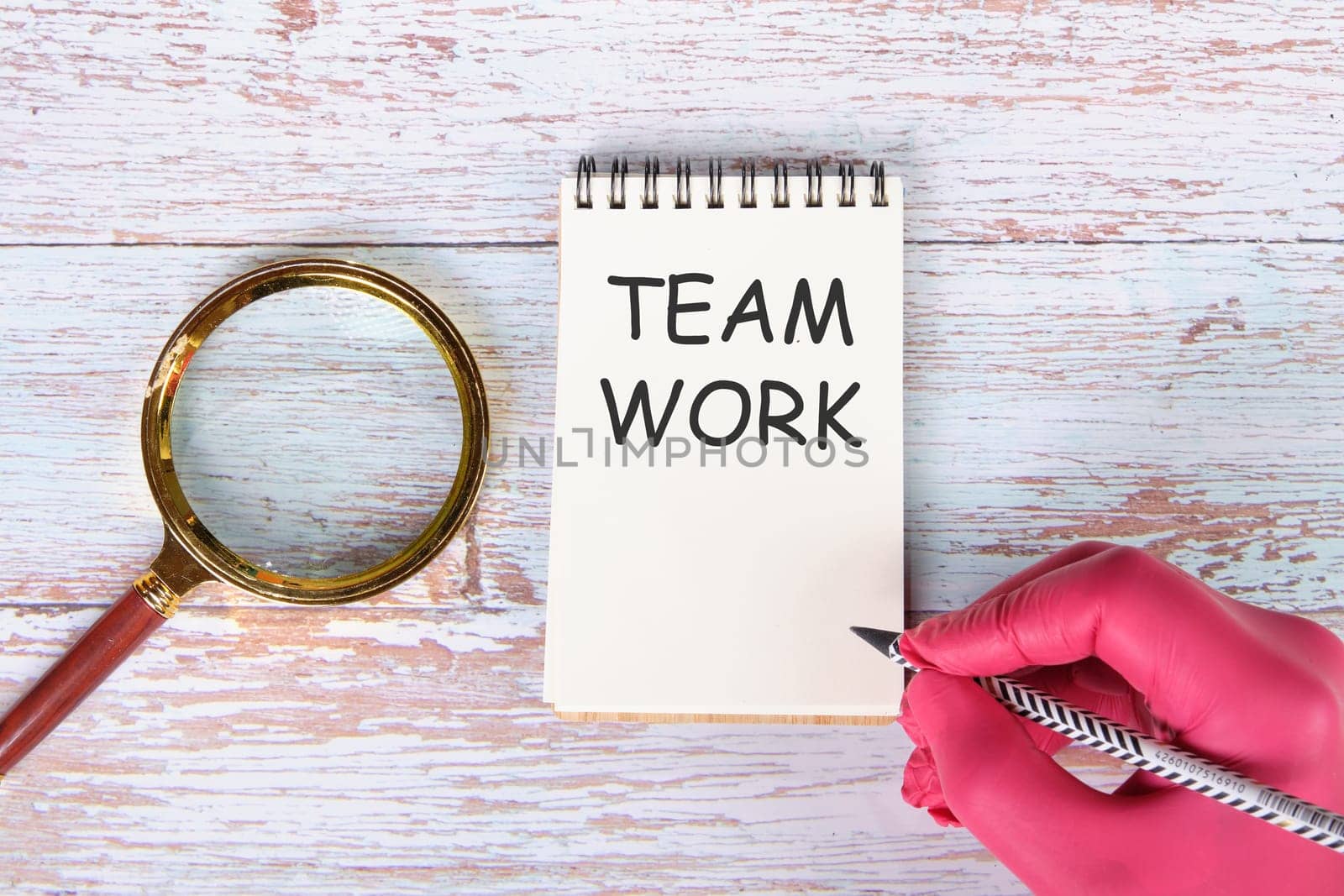 TEAM WORK writing on a notebook lying on old boards next to a magnifying glass and a hand in a red medical glove with a pencil