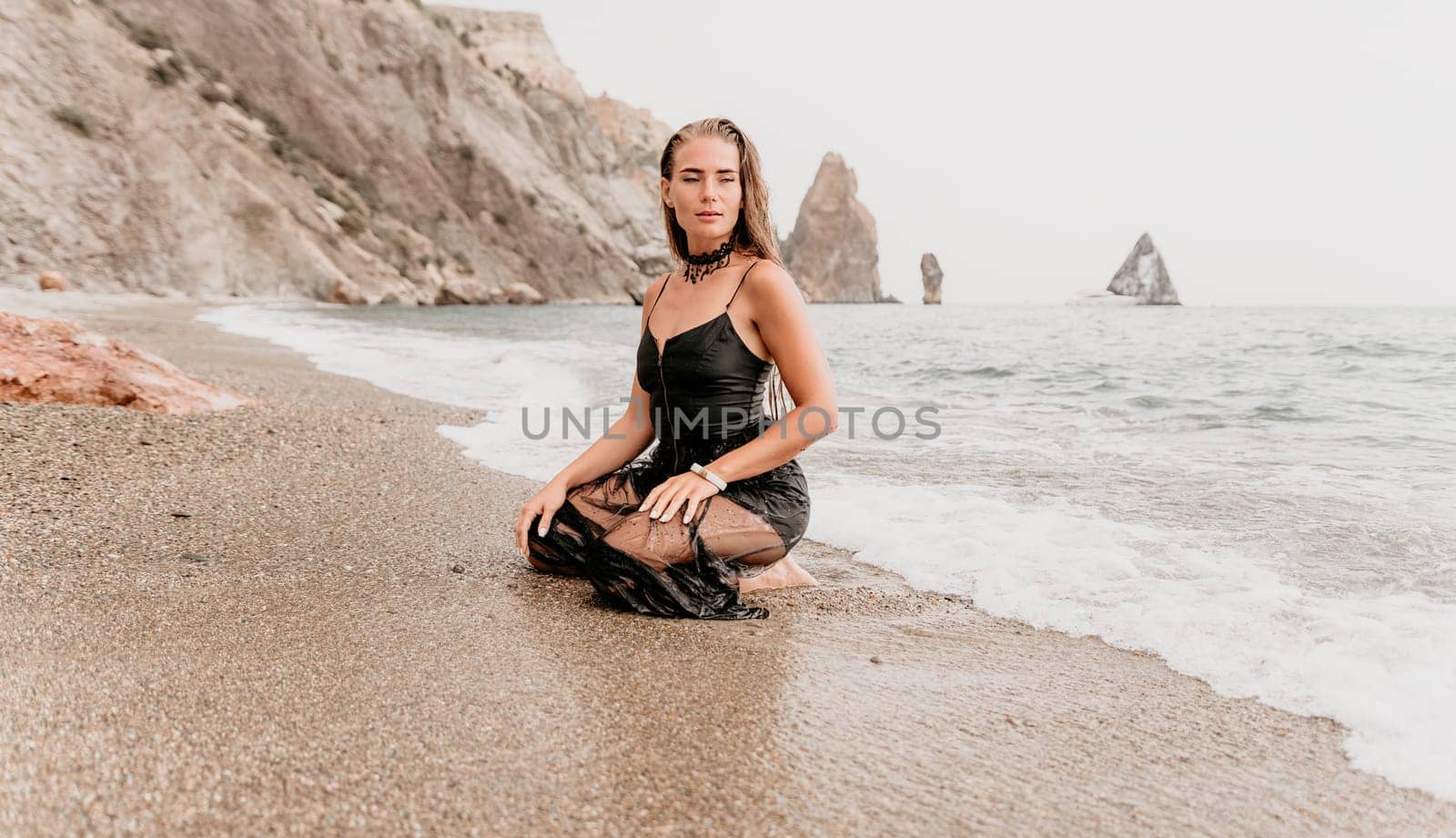 Woman summer travel sea. Happy tourist in black dress enjoy taking picture outdoors for memories. Woman traveler posing on sea beach surrounded by volcanic mountains, sharing travel adventure journey by panophotograph