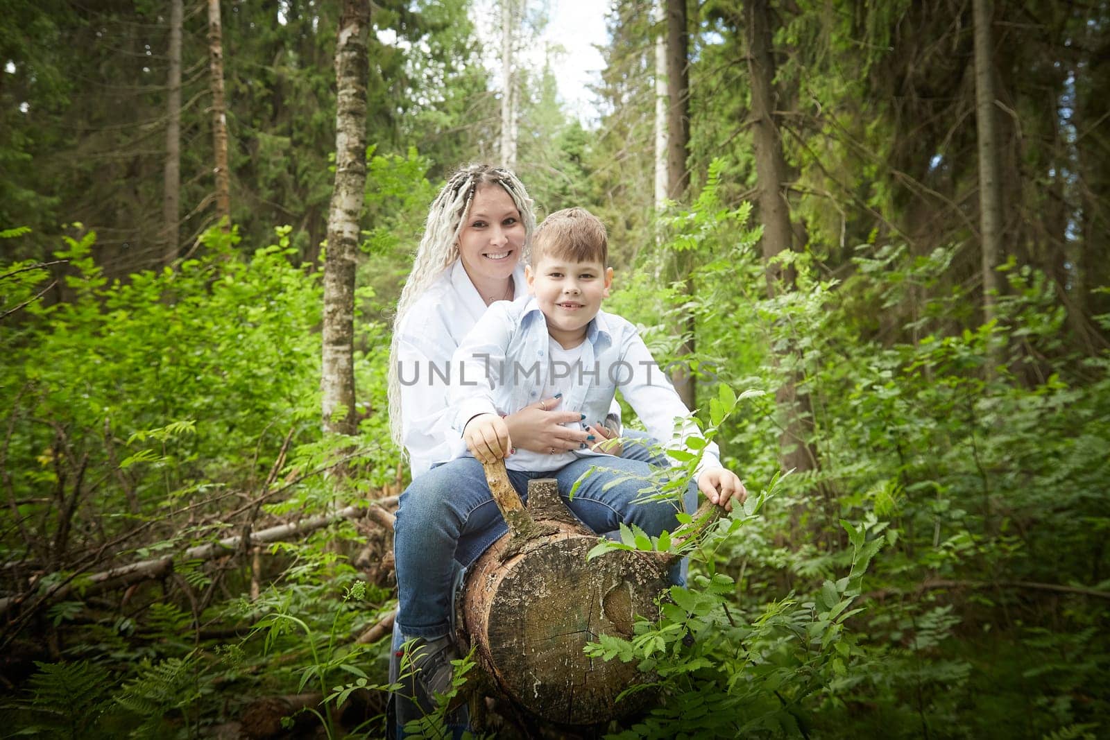 Funny mother with dreadlocks and fat boy happy hugging in forest on a sunny summer day