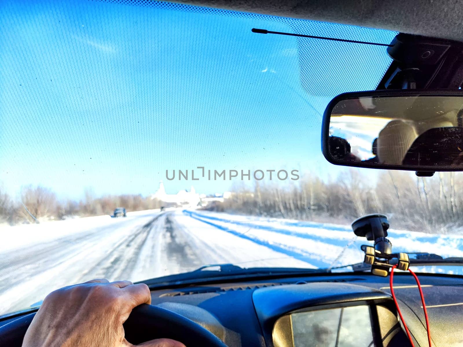 Hand of woman on the steering wheel in car and view through the windshield of a winter road with snow-covered trees