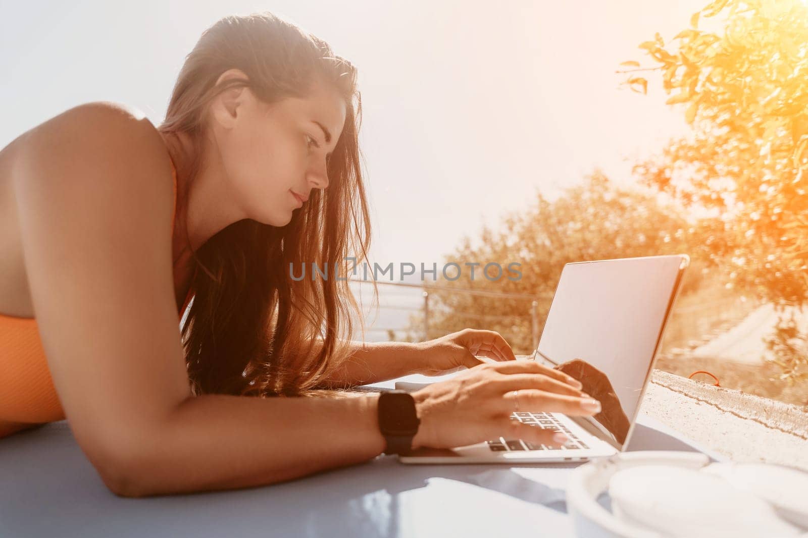 Woman laptop sea. Working remotely on seashore. Happy successful woman female freelancer working on laptop by the sea at sunset, makes a business transaction online. Freelance, remote work on vacation by panophotograph