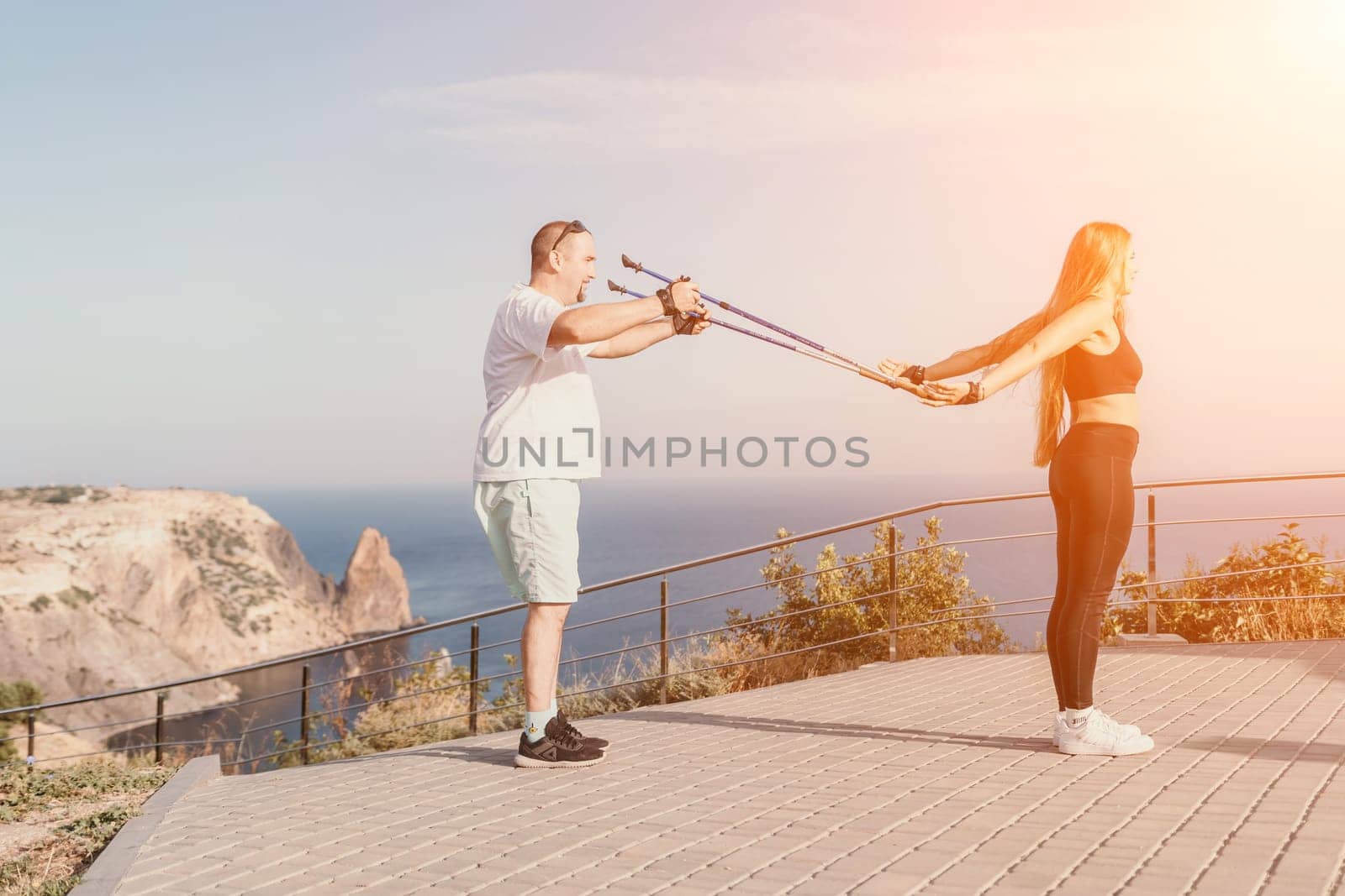 Happy Middle aged couple or friends practicing nordic walking in park near sea. Mature couple with trekking poles walking, practicing Nordic walking outdoors. Aging youthfully and sport concept.