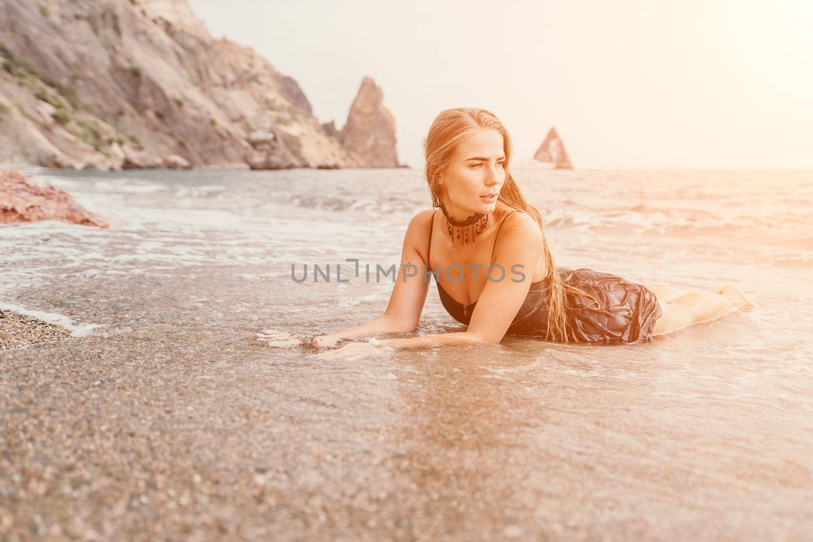 Woman summer travel sea. Happy tourist in black dress enjoy taking picture outdoors for memories. Woman traveler posing on sea beach surrounded by volcanic mountains, sharing travel adventure journey by panophotograph