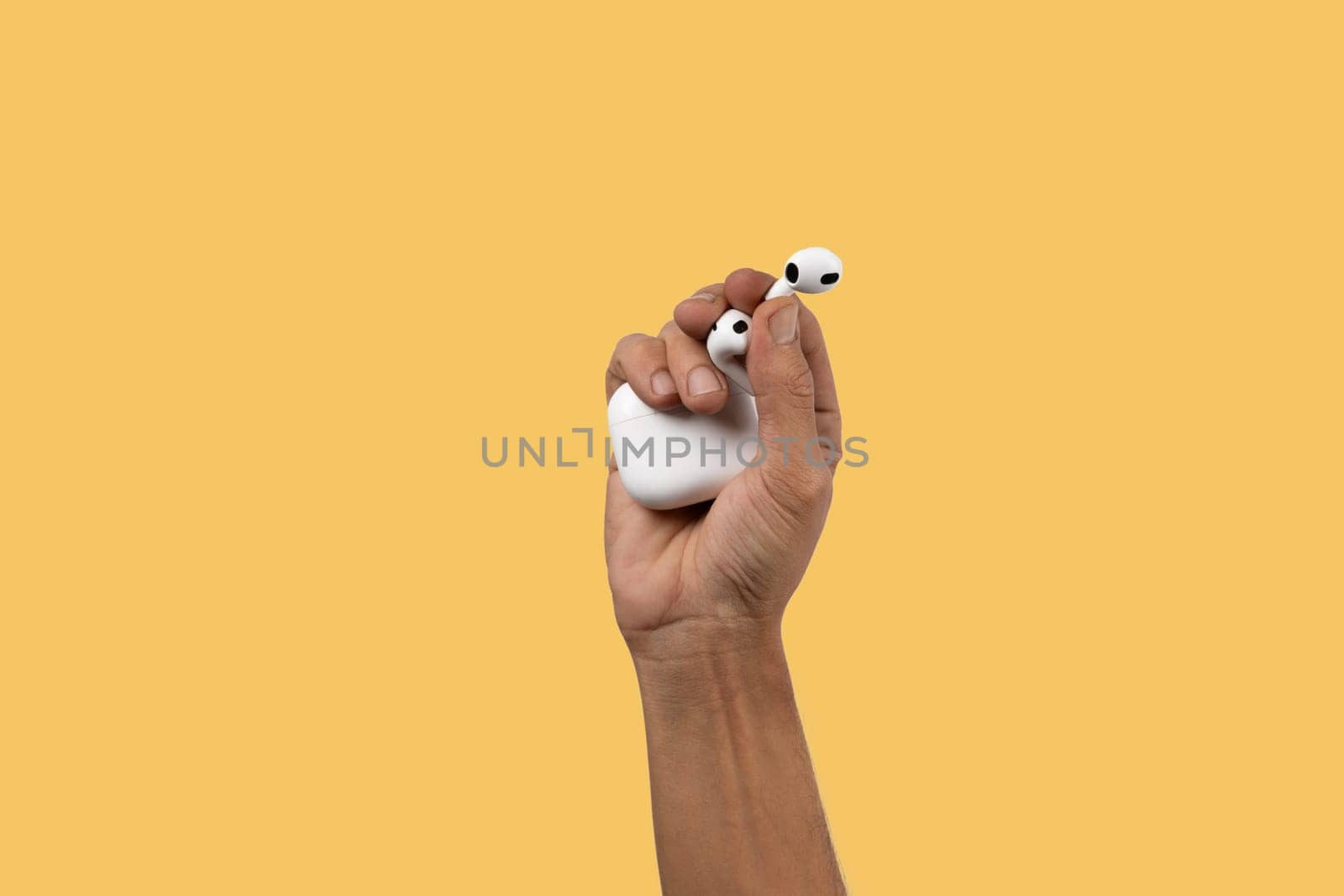 Black male hand holding wireless headphones isolated on yellow. High quality photo