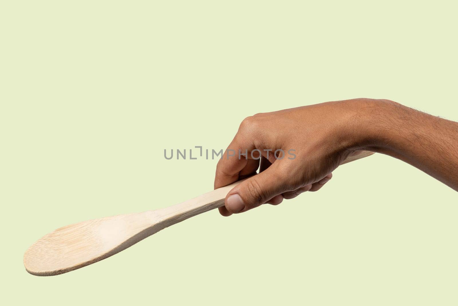 Black male hand holding a wooden cooking spoon isolated on light green background. High quality photo