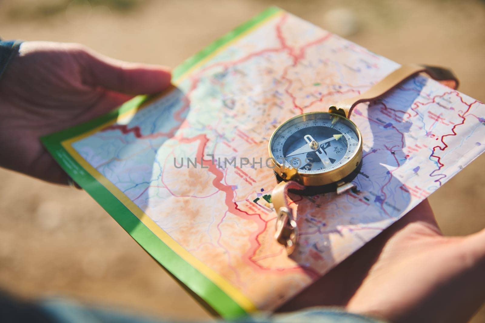 Close-up hands of traveler holding map and using navigational equipment compass, searching north direction while hiking, exploring nature. Travel. Tour tourism. Exploration. Journey. Leisure activity