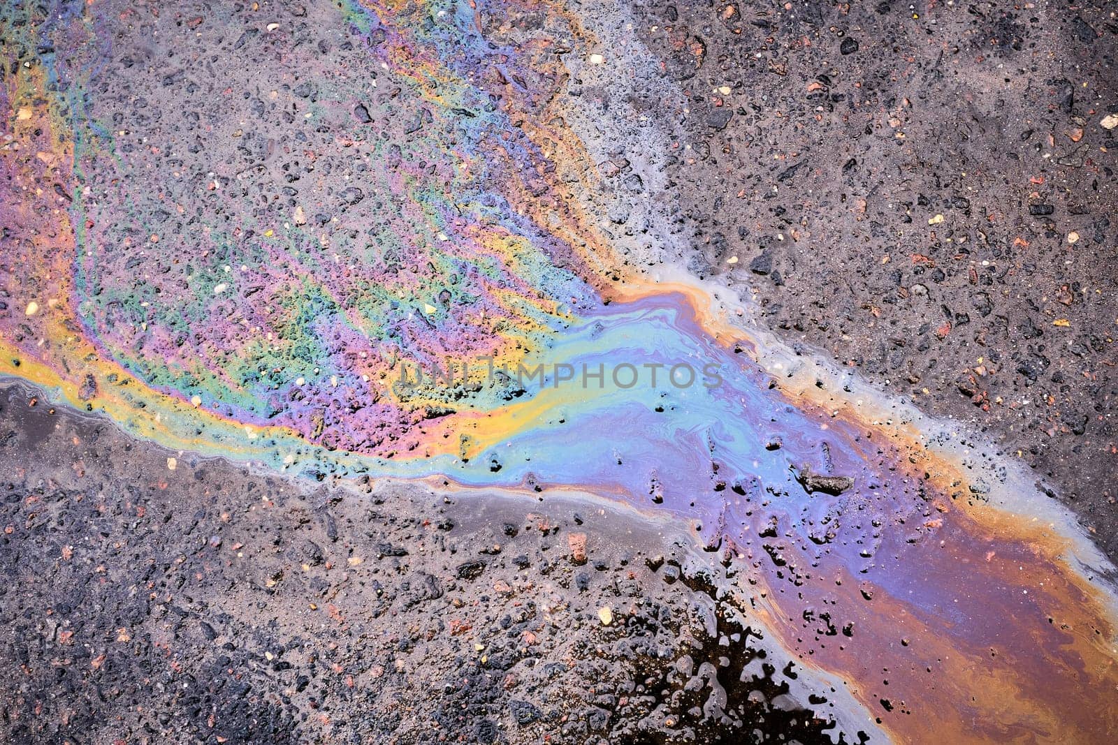 Textured stain of fuel or oil on wet asphalt on a rainy day.