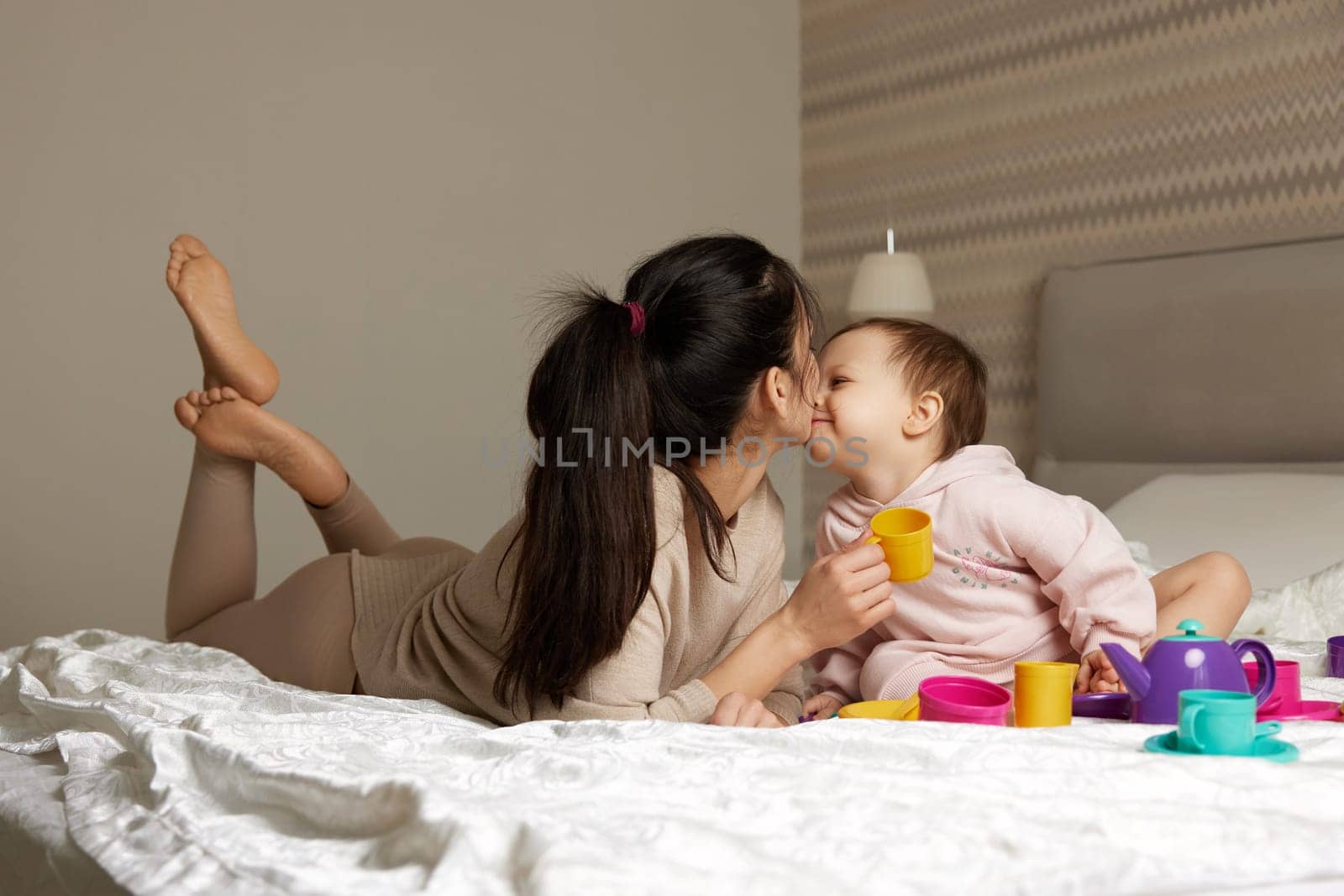mother and little child daughter playing tea party and spending time together in bedroom, family having fun