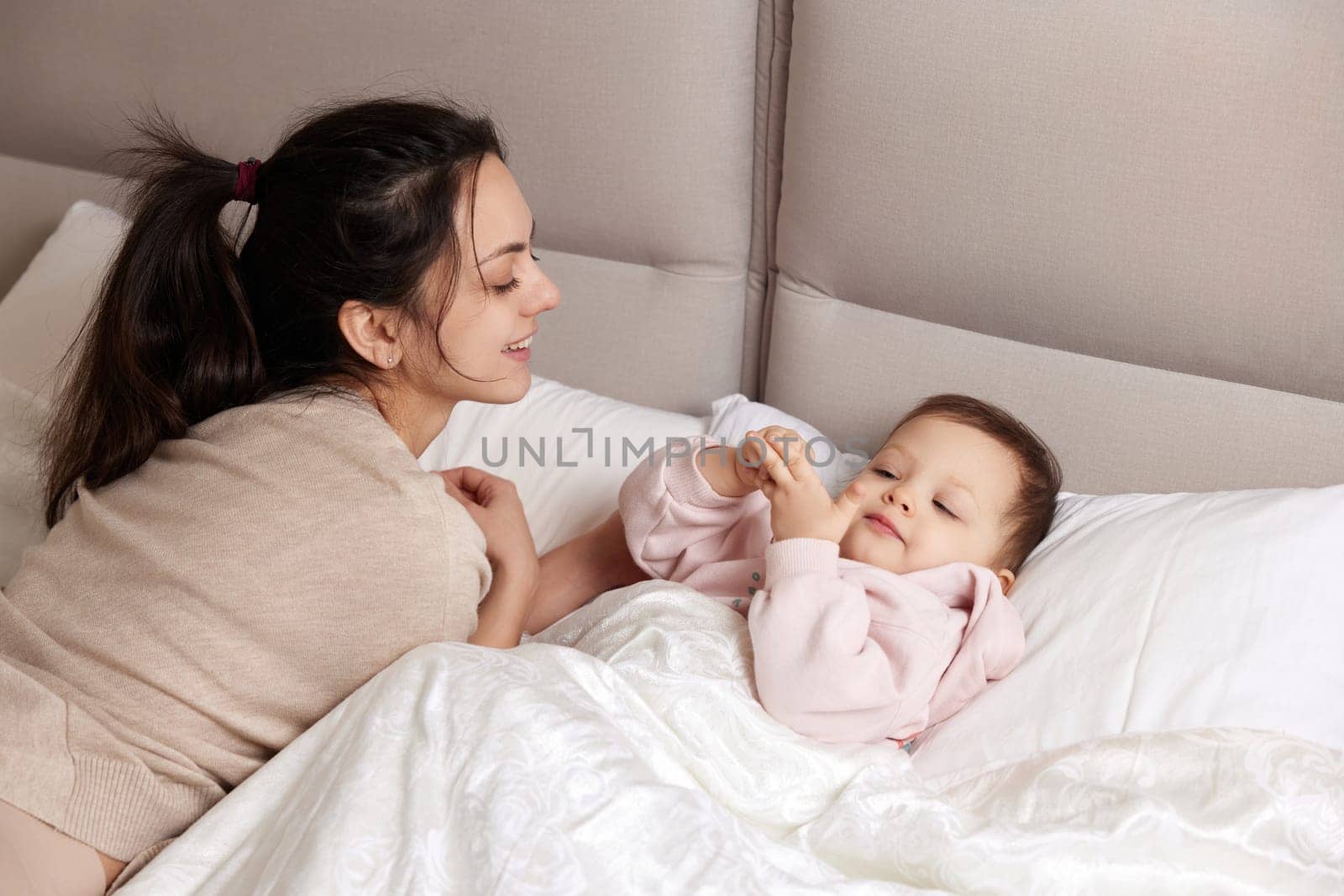 happy mother playing with her cute baby daughter on bed in bedroom. loving family having fun