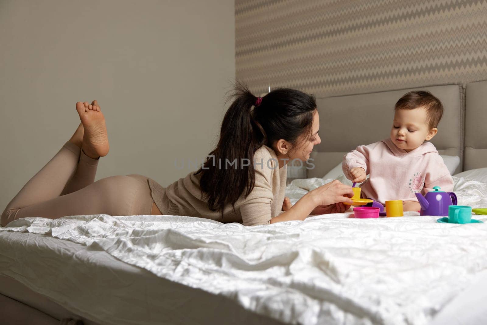 mother and little child daughter playing tea party and spending time together on bed, family having fun,
