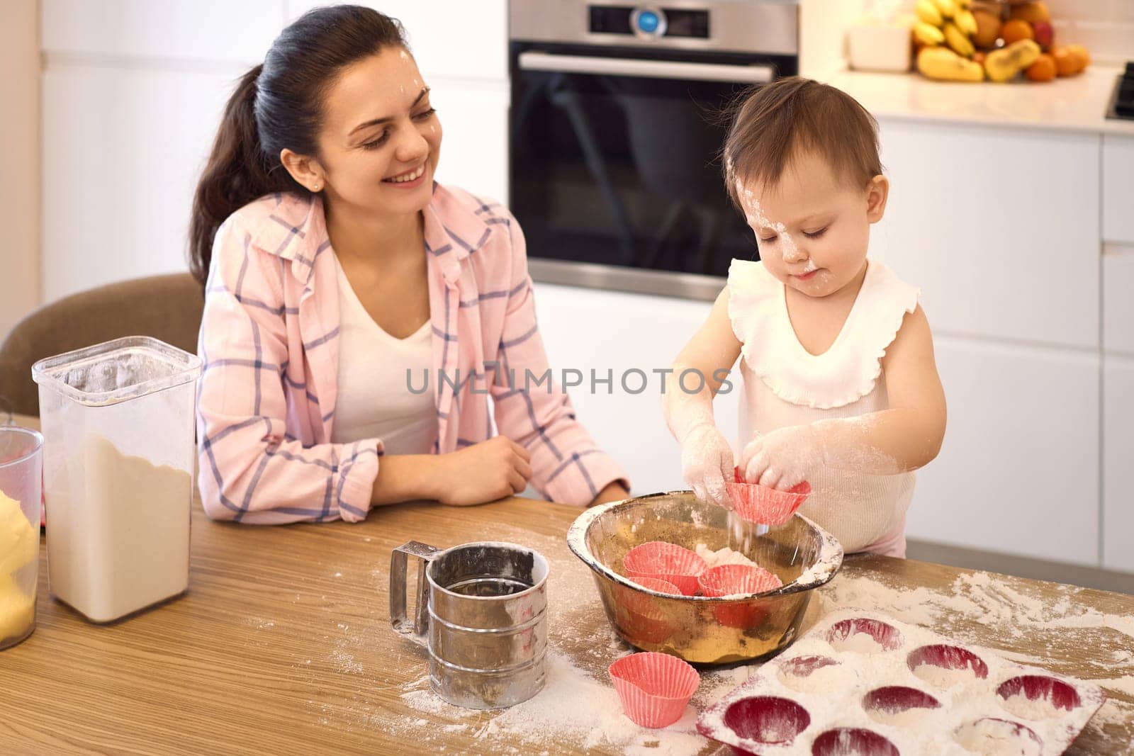 mother and little baby girl preparing the dough in the kitchen, bake cookies. happy time together