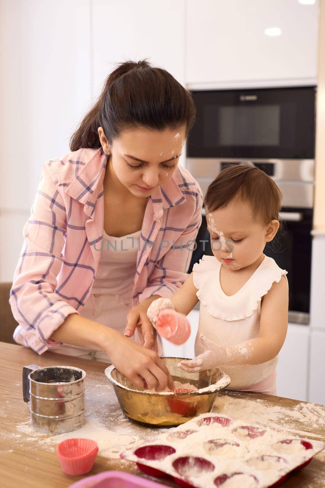 mother and little baby girl preparing the dough in the kitchen, bake cookies. happy time together