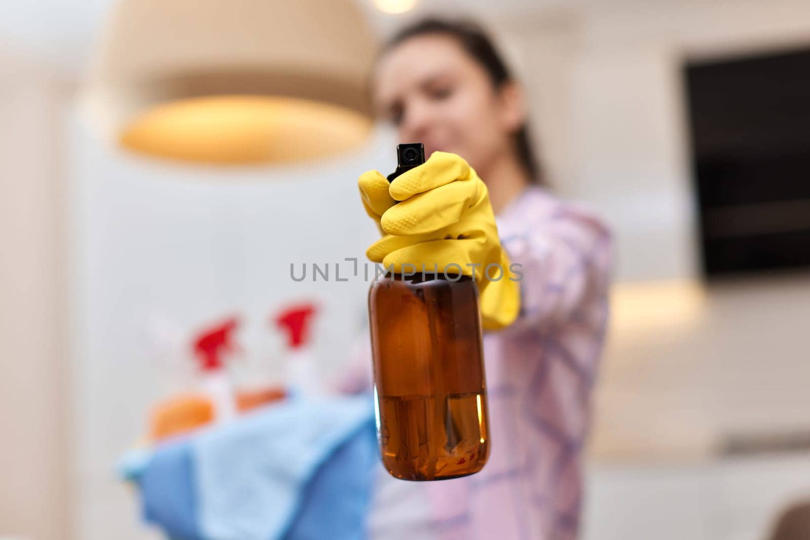 Woman in rubber protective yellow gloves spraying detergent and holding bucket with cleaning tools. house chores. copy space
