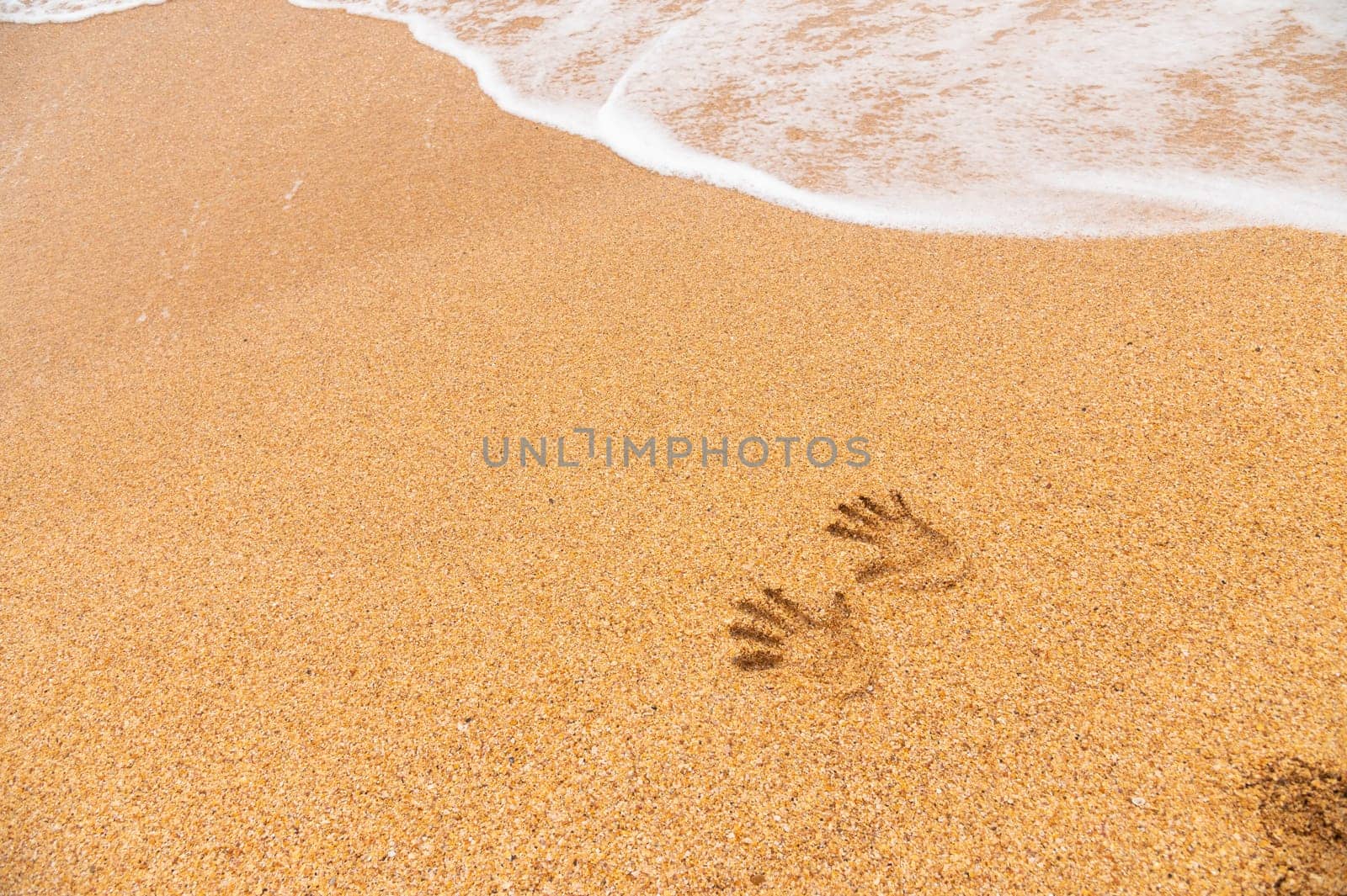 human traces of two hand prints on a sandy beach without people, sea waves rolling in from the side.