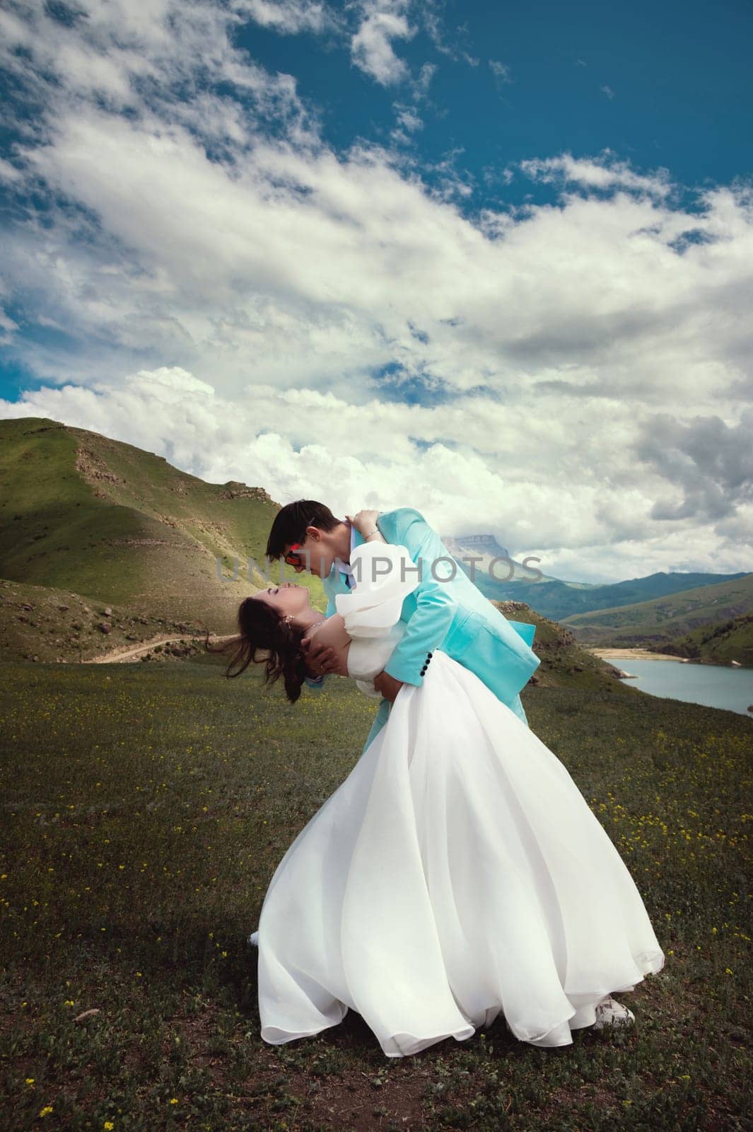 Love, wedding and married couple kissing by the lake outdoors in honor of their romantic marriage. Water, summer, mountains or a kiss.