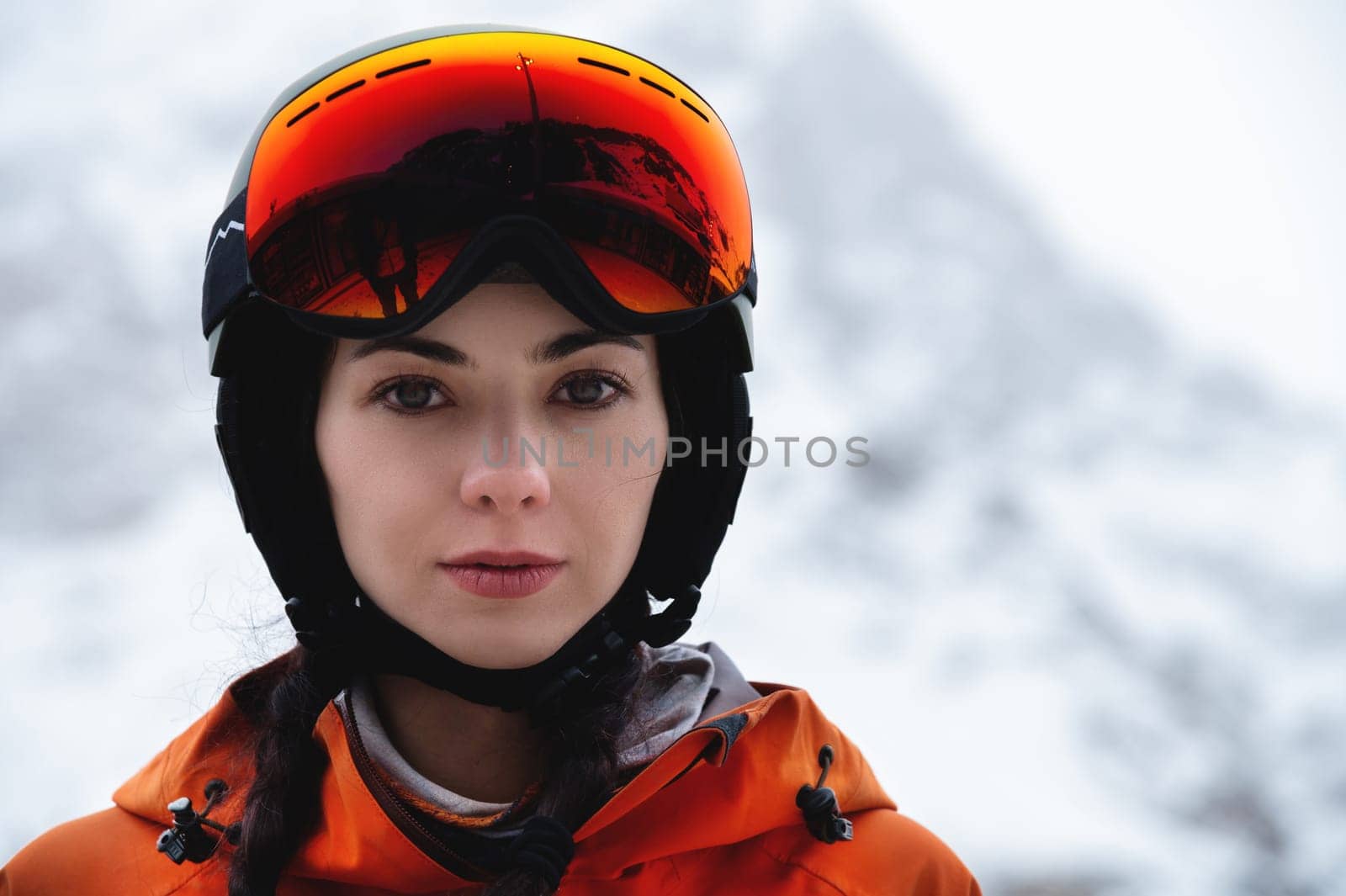 Woman skier on the slope of a mountain resort. Portrait of a young woman smiling in ski equipment, goggles and a helmet.