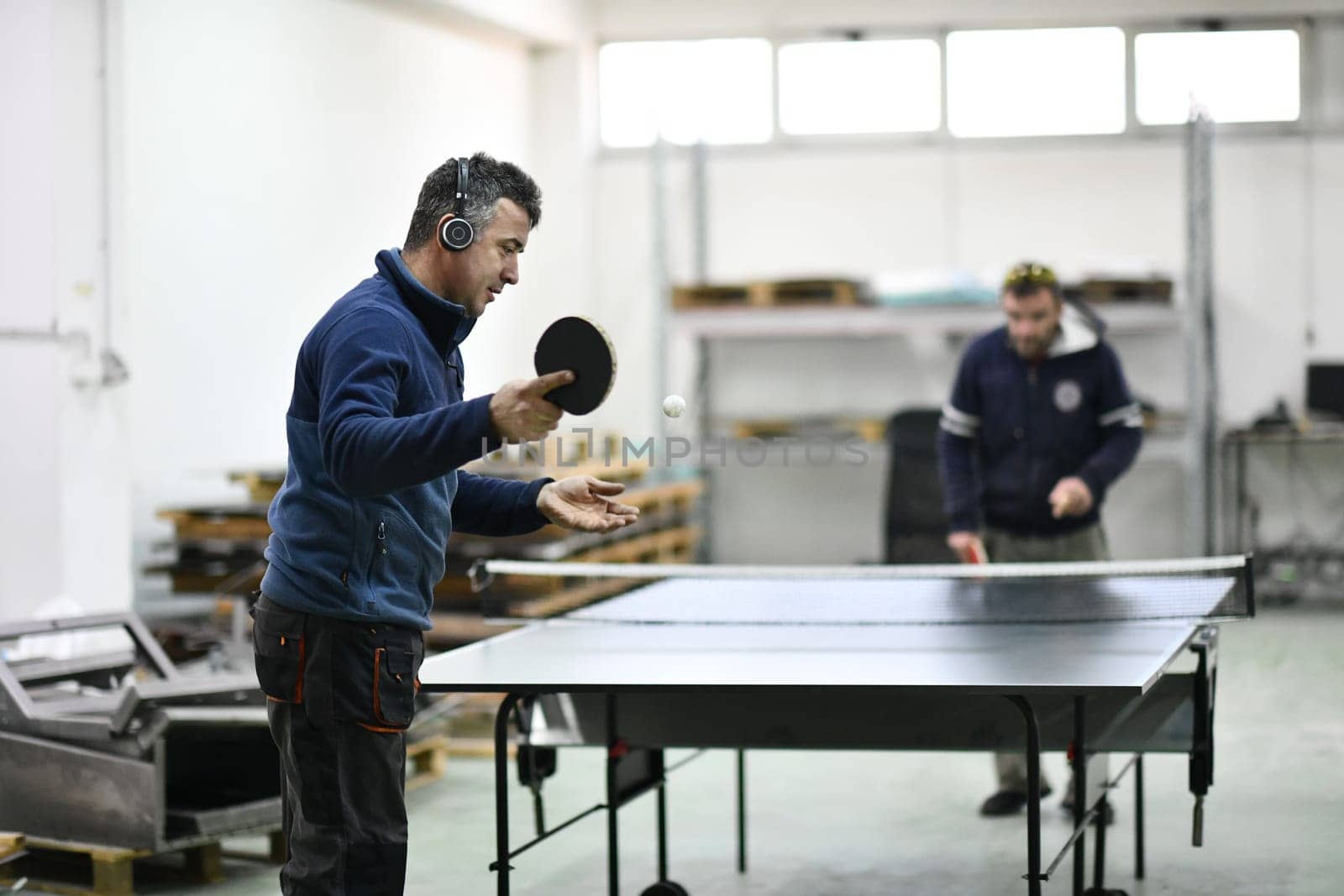 group of industry workers playing ping pong or table tennis game and relaxing in their free time at modern creative metal industry production factory