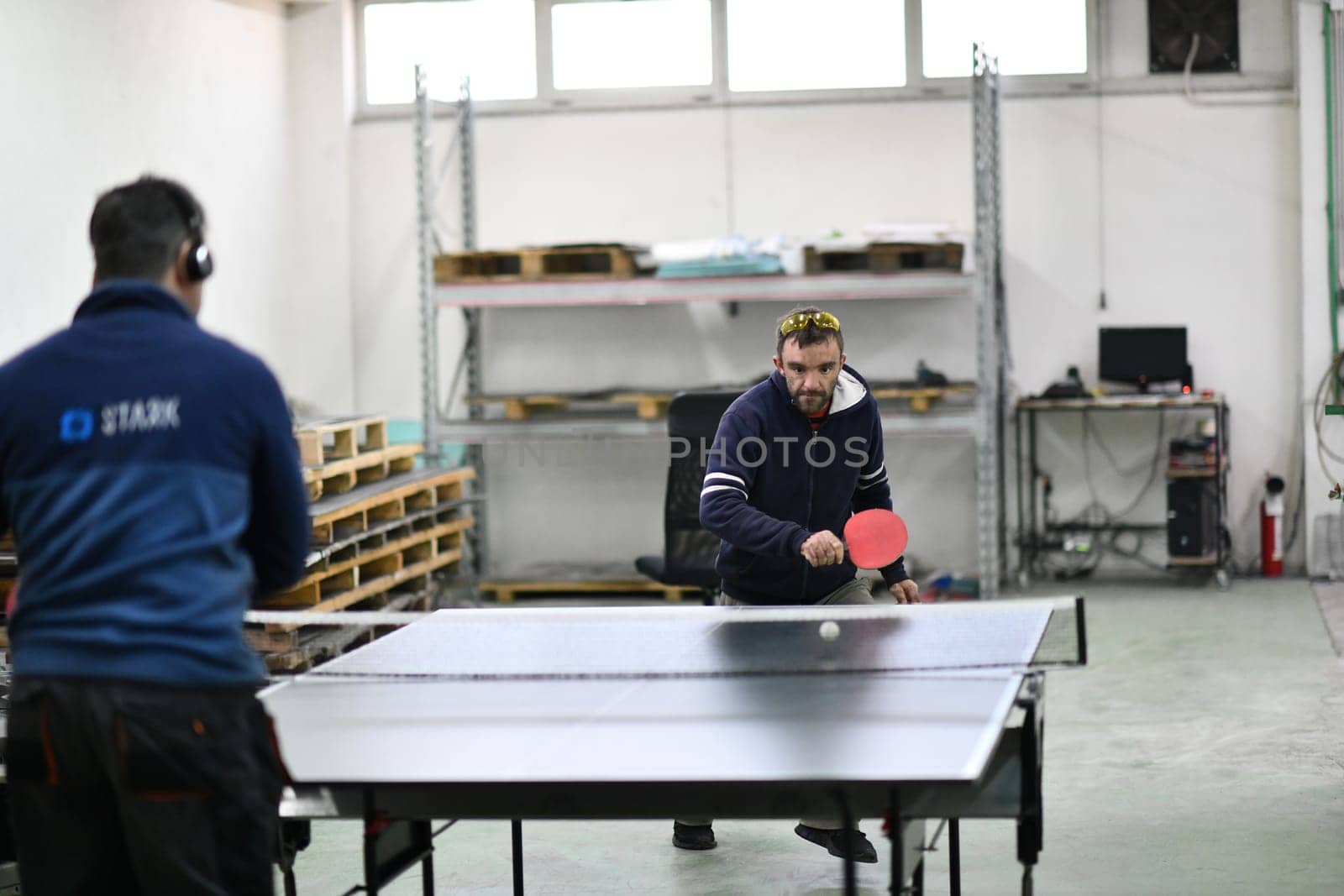 group of industry workers playing ping pong or table tennis game and relaxing in their free time at modern creative metal industry production factory