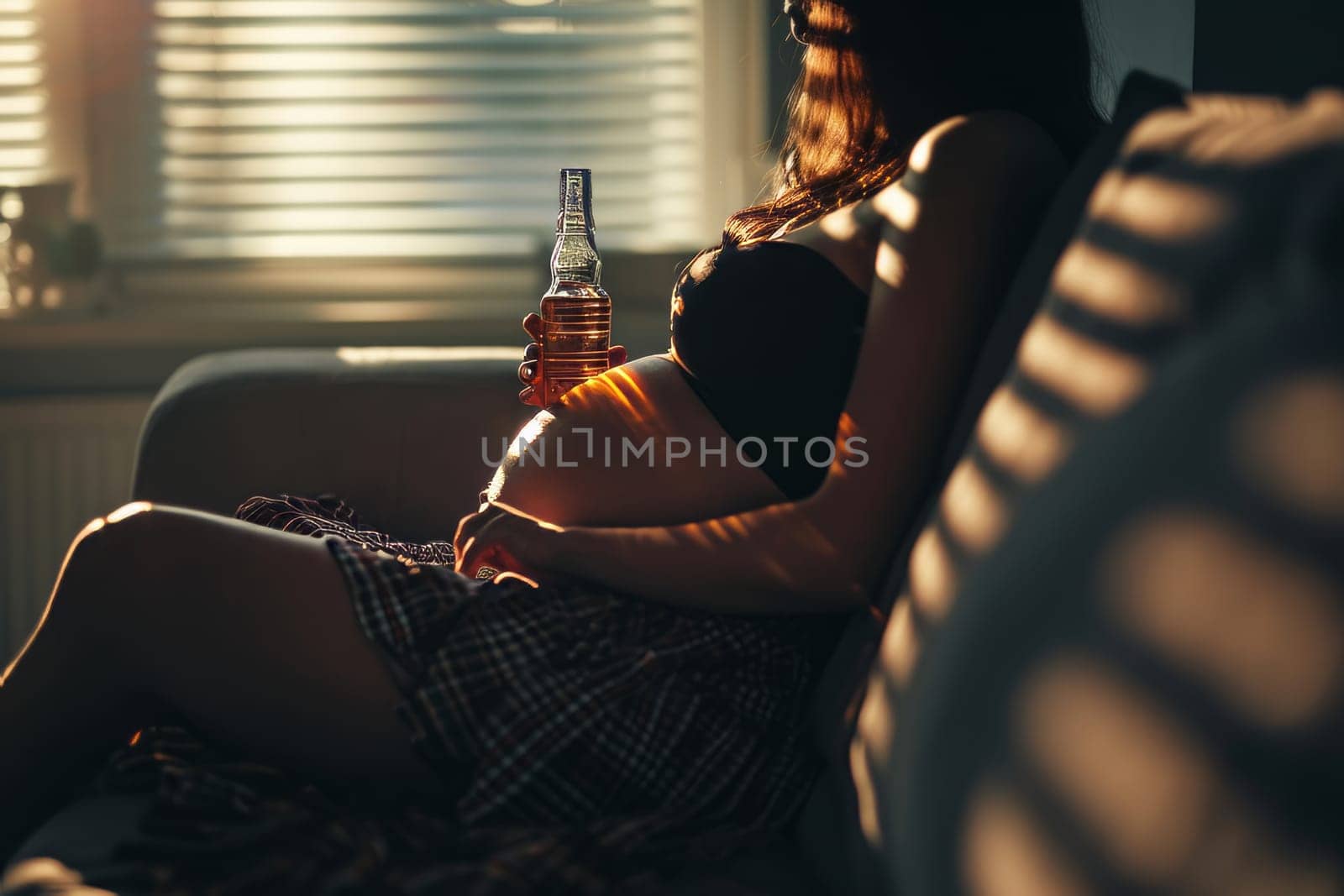 Faceless pregnant woman with bottle of alcohol sitting on the sofa